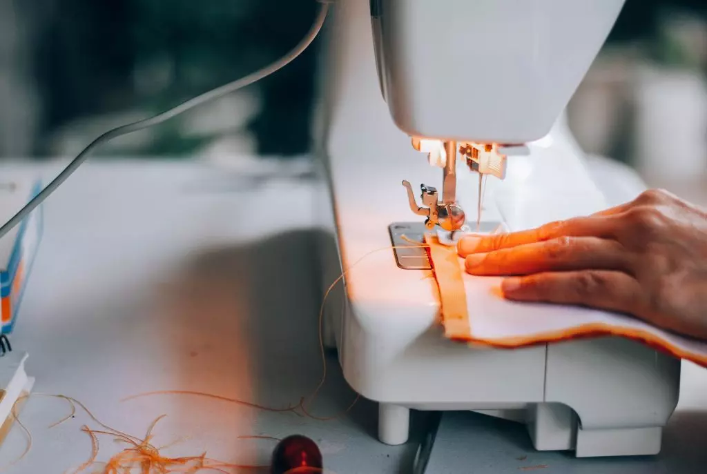 A close-up view of a hand guiding fabric through a sewing machine, highlighting the sewing process.