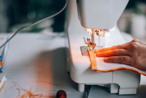 A close-up view of a hand guiding fabric through a sewing machine, highlighting the sewing process.